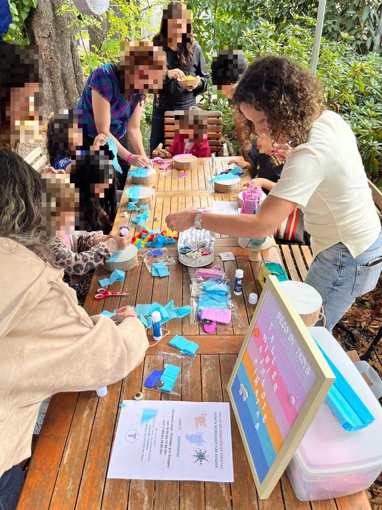 Hands decorating mini piñatas with colorful paper fringe at an outdoor workshop table