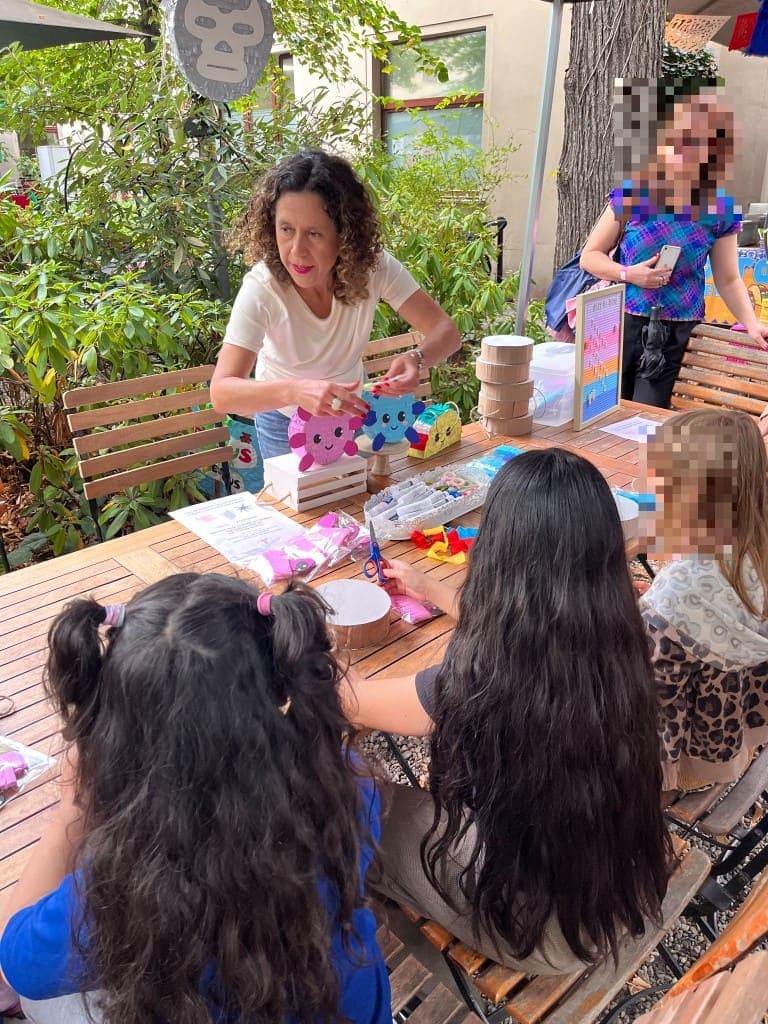 Tatiana guiding children as they decorate mini piñatas at an outdoor workshop table